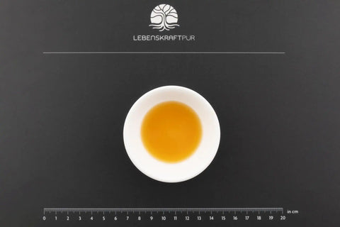 Weiße Schale mit Bio Bitterkräuter Tropfen auf schwarzer Unterlage und Zentimetermaß