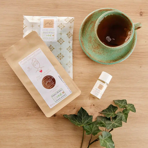 Pflanzenhaarfarbe Set warmes Kupferbraun, Tasse Tee, Pflegeöl und Efeublätter auf Holztisch